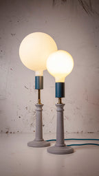 Two table lamps with round light bulbs on light blue stands against a textured industrial white wall.