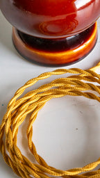 Coiled gold cord on a white surface with a blurred brown object in the background
