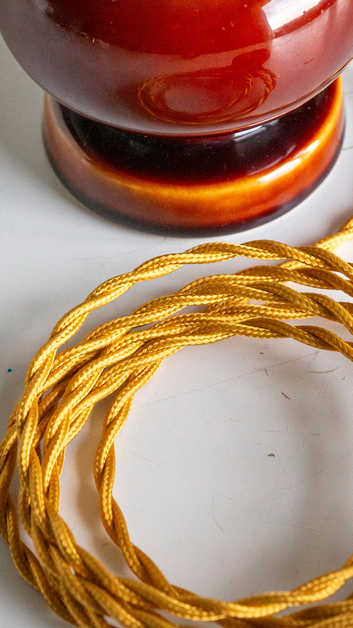 Coiled gold cord on a white surface with a blurred brown object in the background