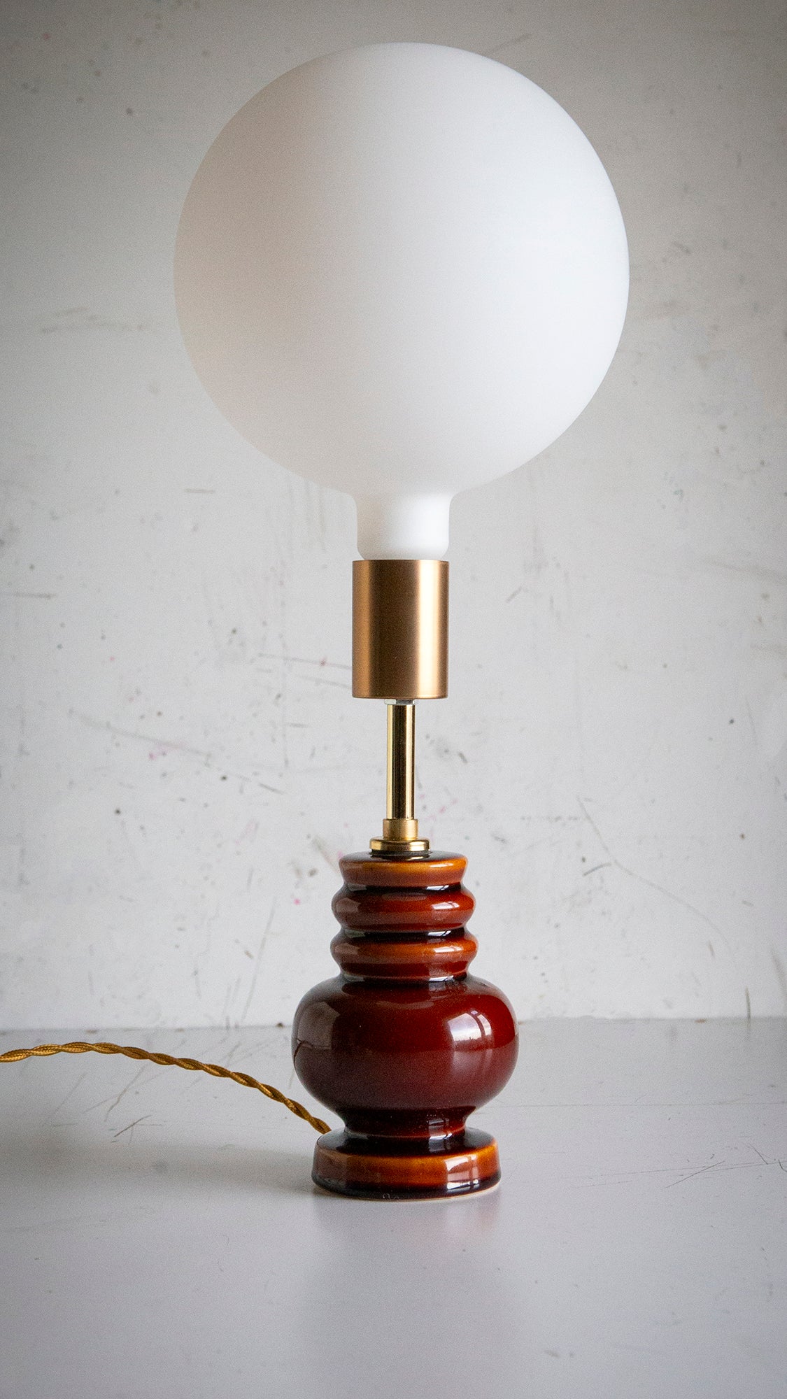 Table lamp with a brown ceramic base and extra large white globe led bulb on a light gray surface.