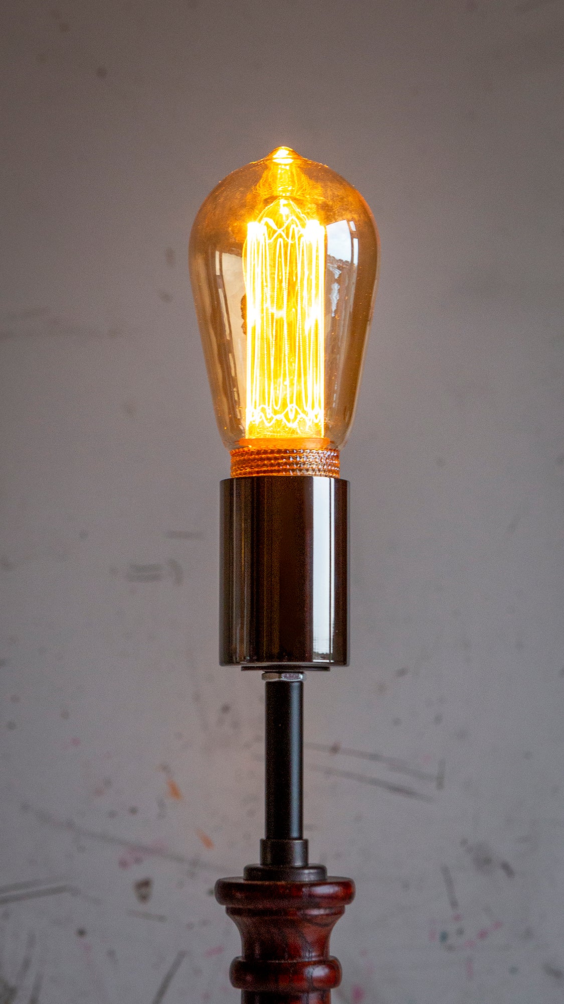 Vintage-style light bulb on a wooden base against a textured gray background